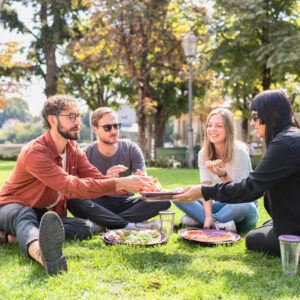 Eine Gruppe von vier Menschen ist zu sehen, sitzend in eine Park, sie essen Pizza aus der reCIRCLE Pizza BOX